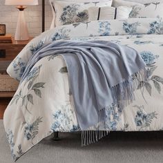 a bed with blue flowers on it in a bedroom next to a night stand and lamp