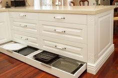 an open drawer in the middle of a kitchen with white cabinets and wood flooring