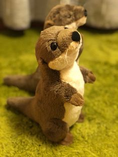 a stuffed animal otter sitting on the ground with its paw in it's mouth