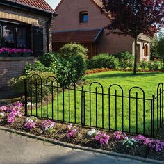 a black iron fence in front of a house with pink and white flowers around it