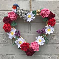 a crocheted heart shaped wreath hanging on a brick wall with flowers in the shape of a bird