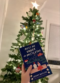 someone holding up a book in front of a christmas tree