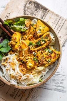 a bowl filled with noodles and vegetables on top of a newspaper next to chopsticks