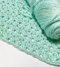 a green crocheted blanket with a ball of yarn next to it on a white surface