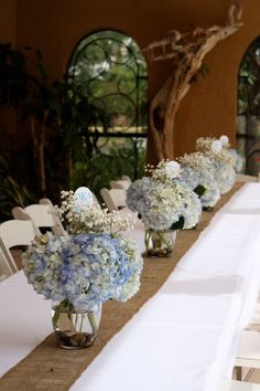 the table is set up with white and blue flowers in vases on top of it