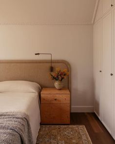 a bedroom with a bed, nightstand and flowers on the table in front of it