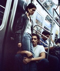 two people sitting on a subway train next to each other with their arms around one another