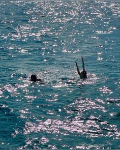 two people swimming in the ocean with their hands up and one person diving into the water