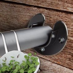 a white bowl filled with green plants next to a metal pipe on a wooden wall