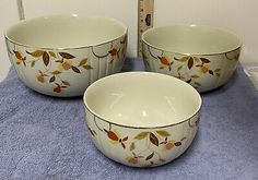 three white bowls with leaves on them sitting on a blue towel next to a ruler