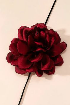 a red flower on a white surface with a black cord attached to it and the petals are very large