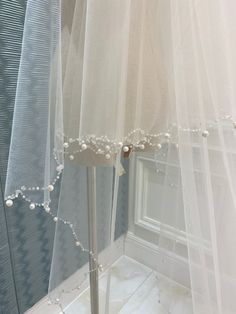 a white veil with pearls hanging from it's side next to a mirror in a room