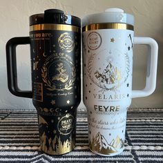 two travel mugs sitting next to each other on top of a carpeted table