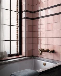 a bath tub sitting next to a window with pink tiles on the walls and floor