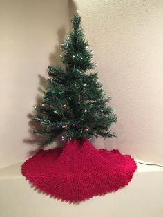 a knitted christmas tree sits on top of a red blanket, which is attached to a white wall