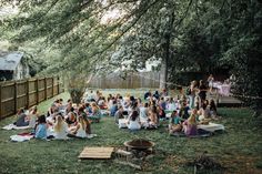 a group of people sitting on top of a lush green field next to a wooden fence