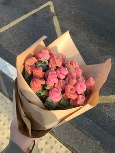 a person holding a brown paper bag filled with pink flowers on top of a sidewalk