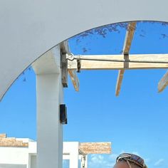 a woman sitting on top of a white bench under a wooden roof next to the ocean