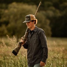 a young man holding a baseball bat and wearing a camo hat in a field