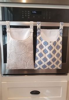 two aprons hanging on the oven door in front of an oven with white and blue curtains