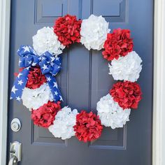 a patriotic wreath with red, white and blue flowers is hanging on the front door