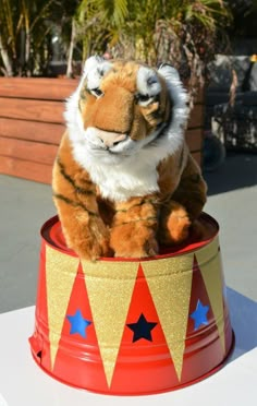 a stuffed tiger sitting in a red and gold tin can with stars on it's sides