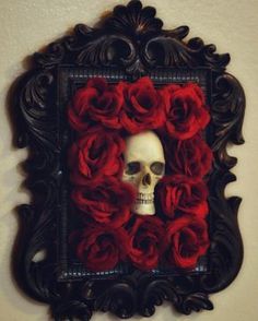 a skull in a frame with red roses on the inside and behind it is a white wall