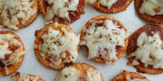 small appetizers with cheese and sauce on them sitting on a white surface, ready to be eaten