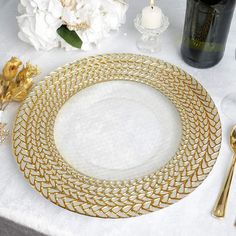 a white table topped with gold plates and silverware next to flowers on top of it