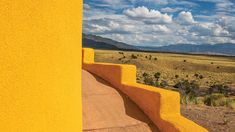 a yellow wall with steps leading up to it and mountains in the distance on a sunny day