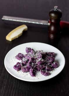 a white plate topped with purple food next to a knife and pepper shaker on top of a table