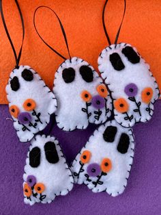 four white and orange felt ornaments hanging from strings on purple surface with orange wall in background