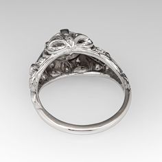 This gorgeous circa 1930s Art Deco engagement ring features a pierced and engraved design and milgrain details. The ring is centered with a 1.30 carat round transitional brilliant cut diamond, in a four-prong setting. The diamond is GIA certified M color and VS1 clarity. The top of the ring is bead set with 16 round single cut diamonds. The shoulders are each channel set with two square step cut lab created sapphires. The ring measures 9.9mm at the top and rises 7.6mm above the finger. The ring is currently a size 6 and we offer complimentary resizing to fit. The ring is platinum and the shank was replaced some time ago with sturdy 14k white gold and looks great. Classic Filigree Diamond Promise Ring, Heirloom Platinum Engraved Ring With Diamond Cut, Antique Formal Cluster Ring With Center Stone, Antique Cluster Ring With Center Stone For Formal Occasions, Platinum Filigree Ring With Center Stone For Formal Occasions, Formal Platinum Filigree Ring With Center Stone, Vintage Engraved Ring With Filigree, Classic White Gold Engraved Ring, Victorian Style Cluster Ring For Anniversary With Round Cut