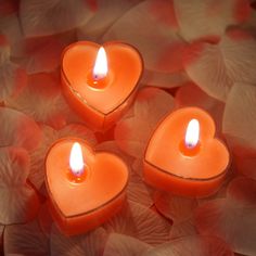 three heart shaped candles sitting on top of petals