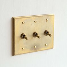 a square brass plate with three knobs on it's side, mounted to a white wall