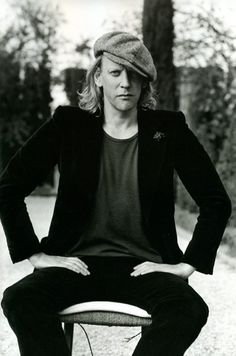 a man sitting on top of a chair with his hands on his hips and wearing a hat