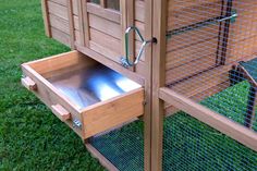 a close up of a chicken coop with the door open and drawers opened on grass