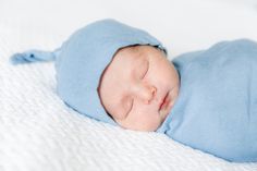 a newborn baby is wrapped in a blue blanket on a white blanketed surface, with his eyes closed