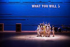 dancers in front of a blue wall with what you will's written on it