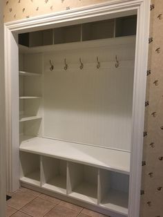 an empty white closet with shelves and hooks on the wall next to a tiled floor