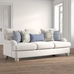 a white couch with blue and gray pillows on it in front of a wooden floor