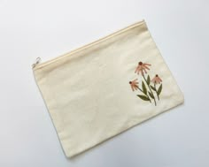 a small pouch with flowers embroidered on the front and side, sitting on a white surface