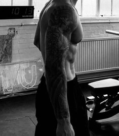 a man standing in front of a window with his back turned to the camera and tattoos on his arms