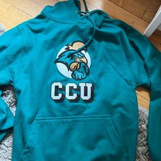 Coastal Carolina Hoodie. Never Worn. Dark Green/Blue Color. Size Small. Blue Graphic Print Sweatshirt For Team Spirit, Blue Varsity Hoodie For Fall, Blue Hooded Top For College, Blue Tops For Campus In Fall, Blue Fan Apparel Sweatshirt For Fall, Blue Graphic Print Sweatshirt For Campus, Blue Team Spirit Sweatshirt For Sports Season, Varsity Blue Sweatshirt For Campus, Blue Crew Neck Hoodie For College