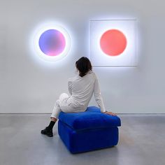 a woman sitting on top of a blue couch in front of two colorful circles mounted to the wall