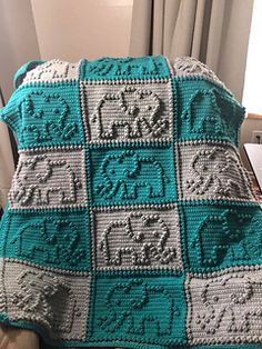 a crocheted blanket with elephants on it sitting on a couch next to a window