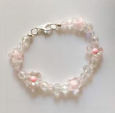 a white bracelet with pink flowers and clear glass beads on a white surface, the bead is attached to a silver clasp