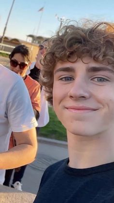 a young man smiling at the camera with other people in the back ground behind him