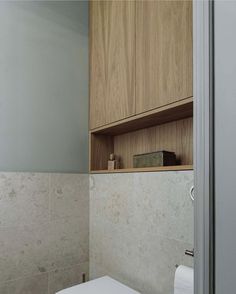 a white toilet sitting in a bathroom next to a wooden cabinet above it's door