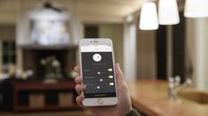 a person holding up a smart phone in a room with wood floors and lights on the ceiling